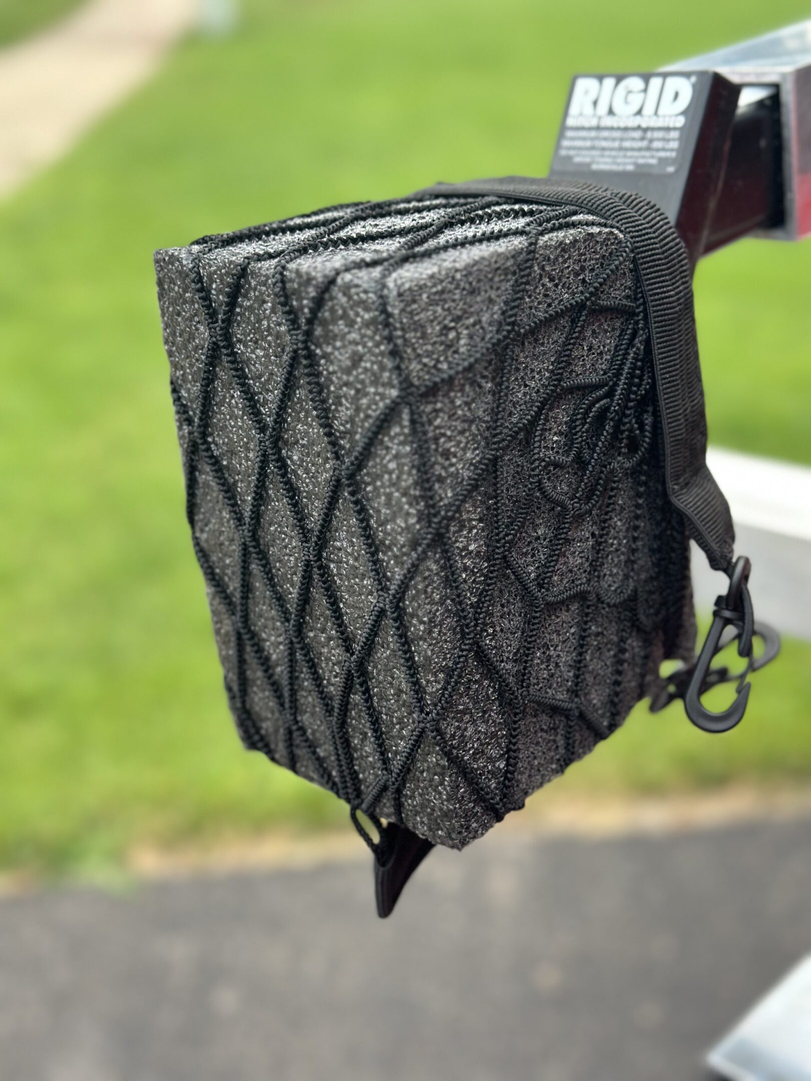 Black fabric-covered object secured with a netting, hanging outdoors.