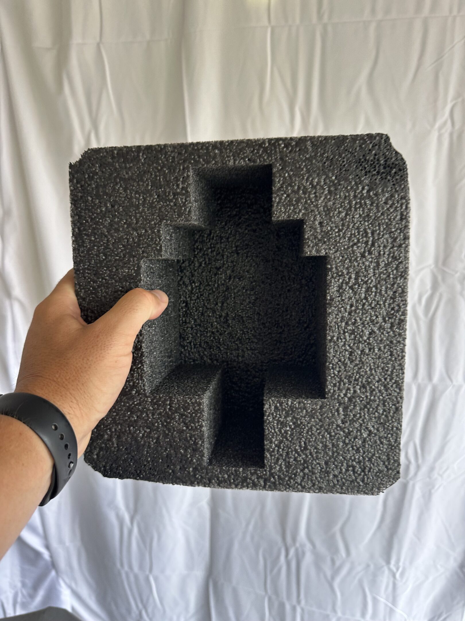 Hand holding a black foam packaging insert with multiple compartments.