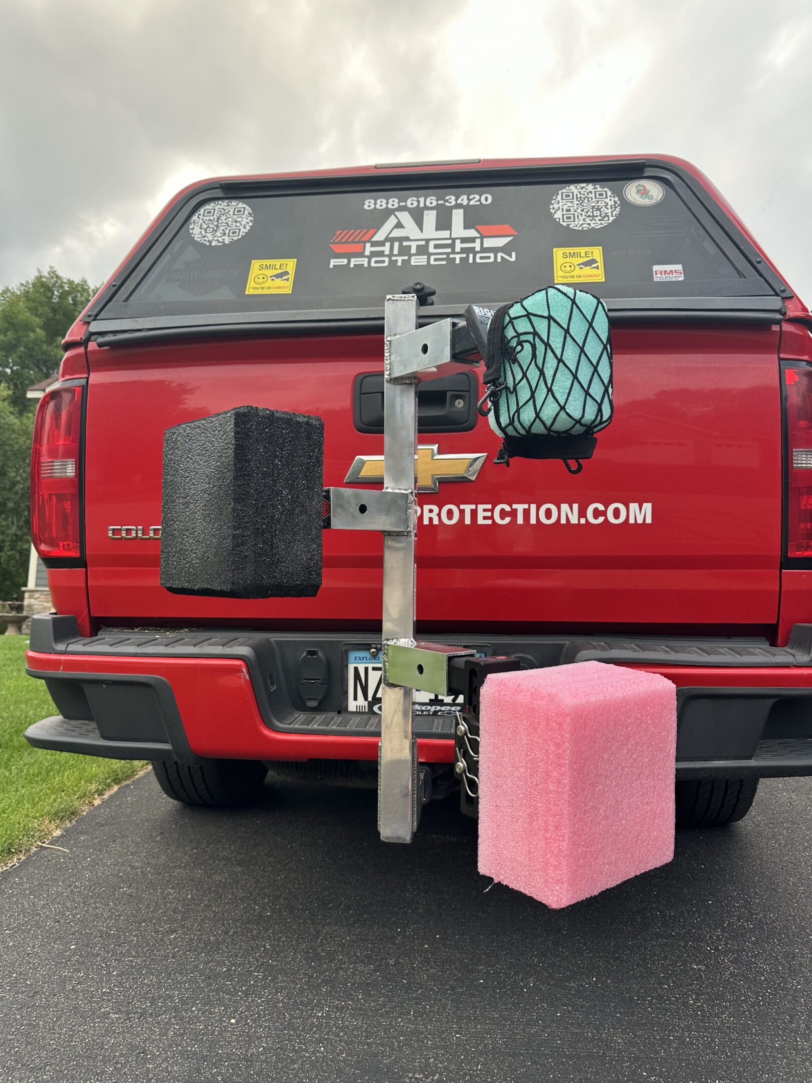 A red truck with three foam blocks attached to a vertical wooden board on its rear.