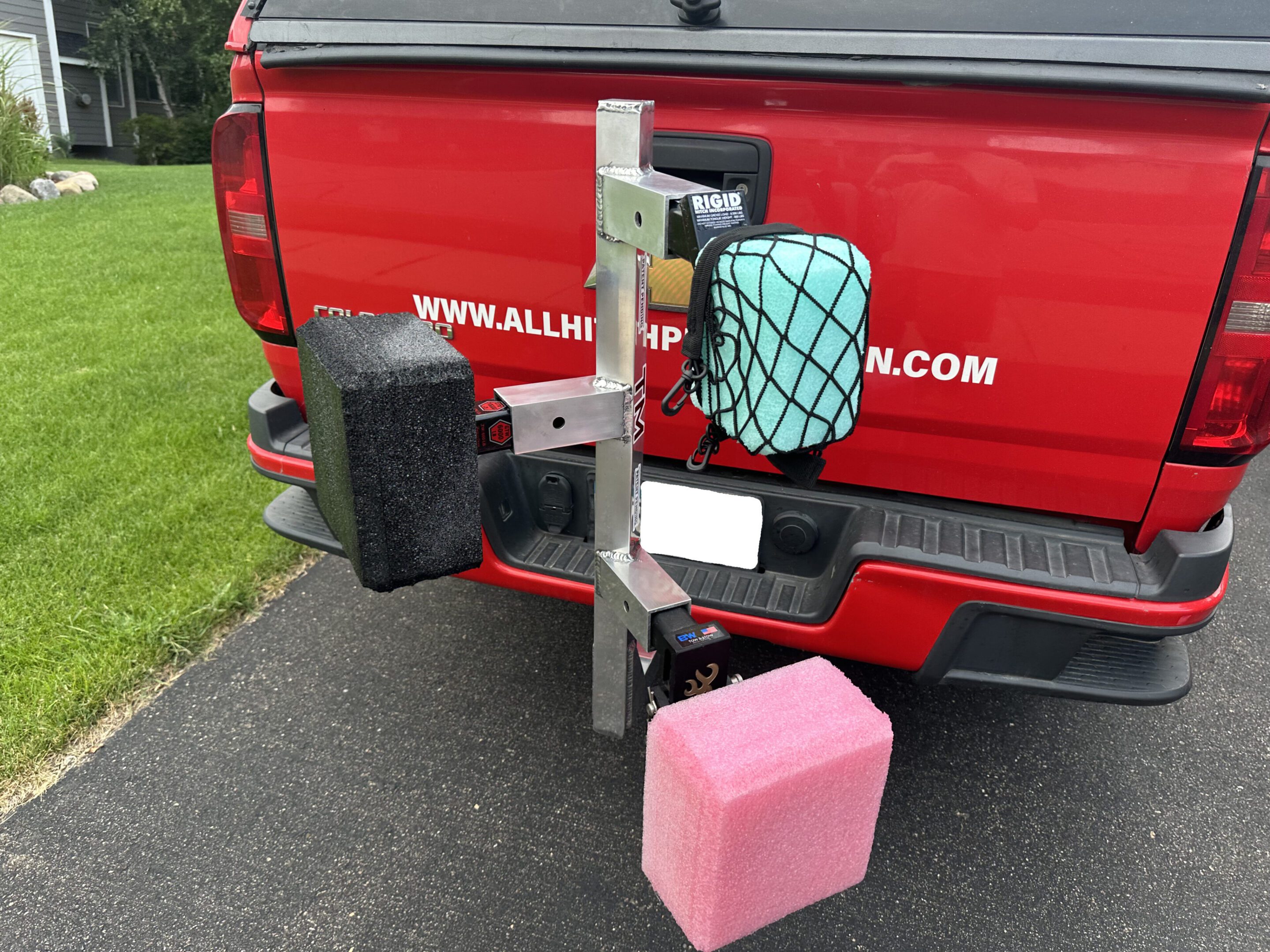 A red truck with a mounted holder carrying a black grill and a pink fuel container.