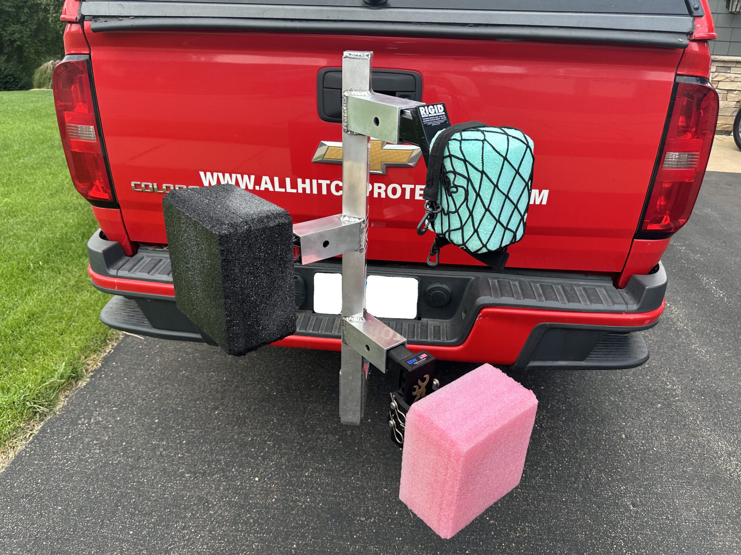 Plastic foam blocks attached to a red vehicle’s rear bumper with straps.