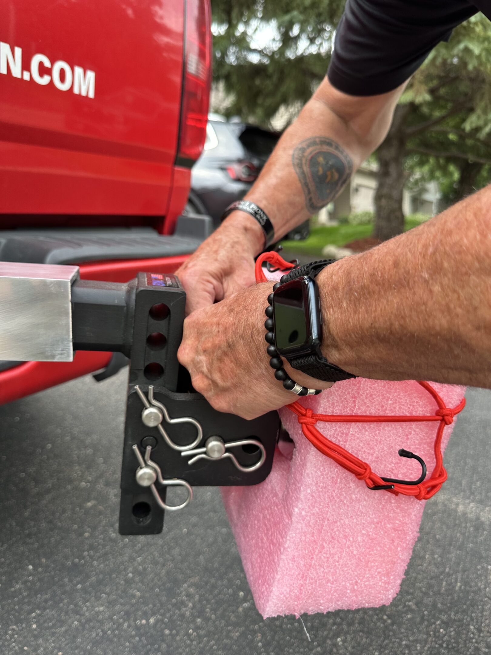 Person securing a pink kayak to a vehicle with a lock and strap.