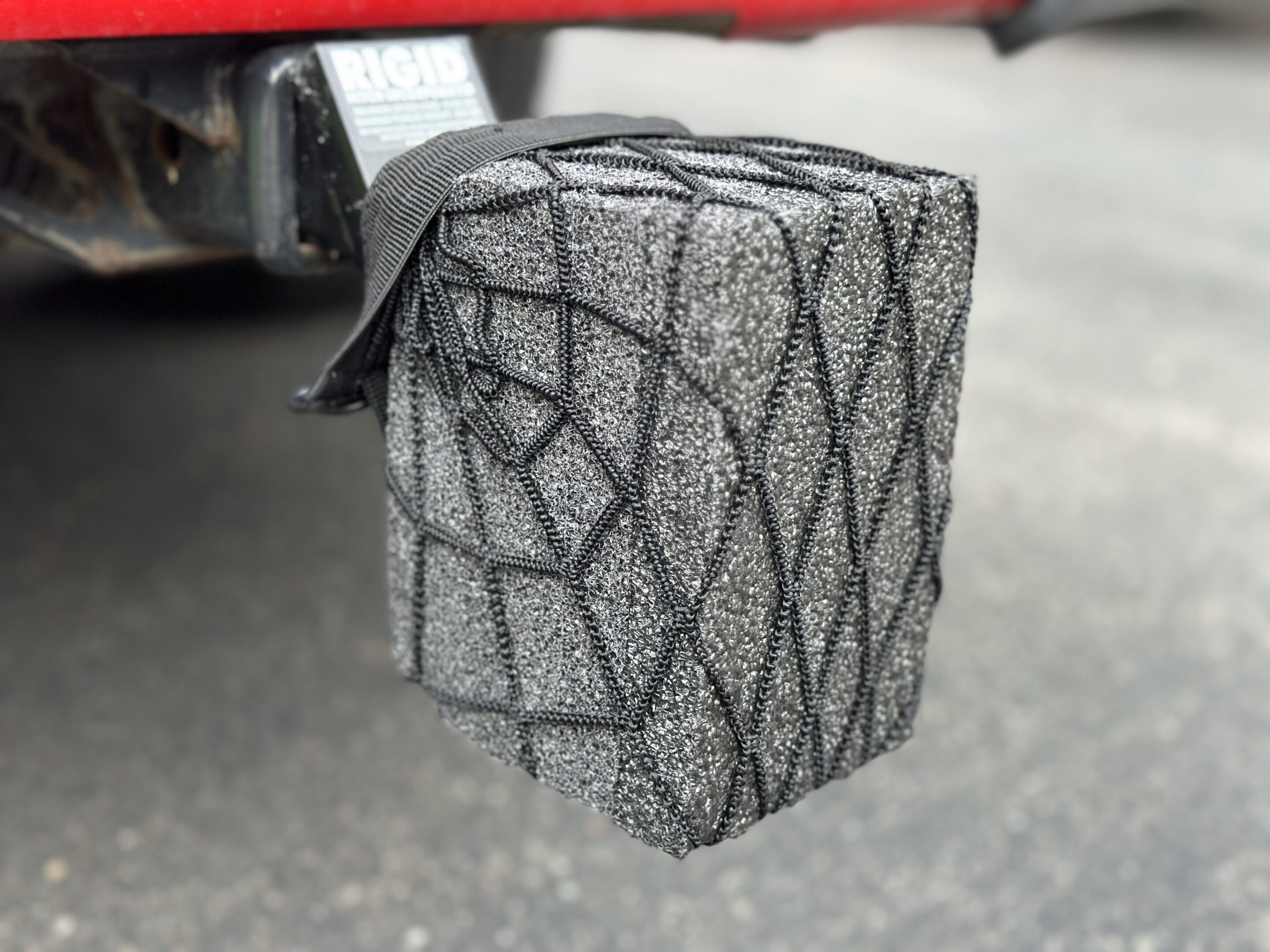A black mesh net securing a gray box on a vehicle's rear.