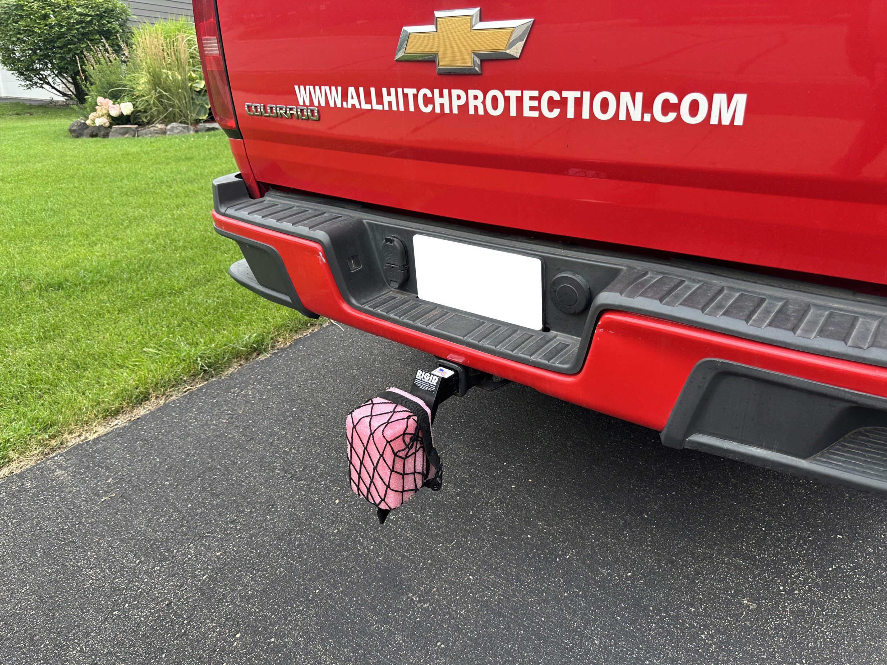 A hitch cover shaped like a pink pig attached to a red truck's trailer hitch.