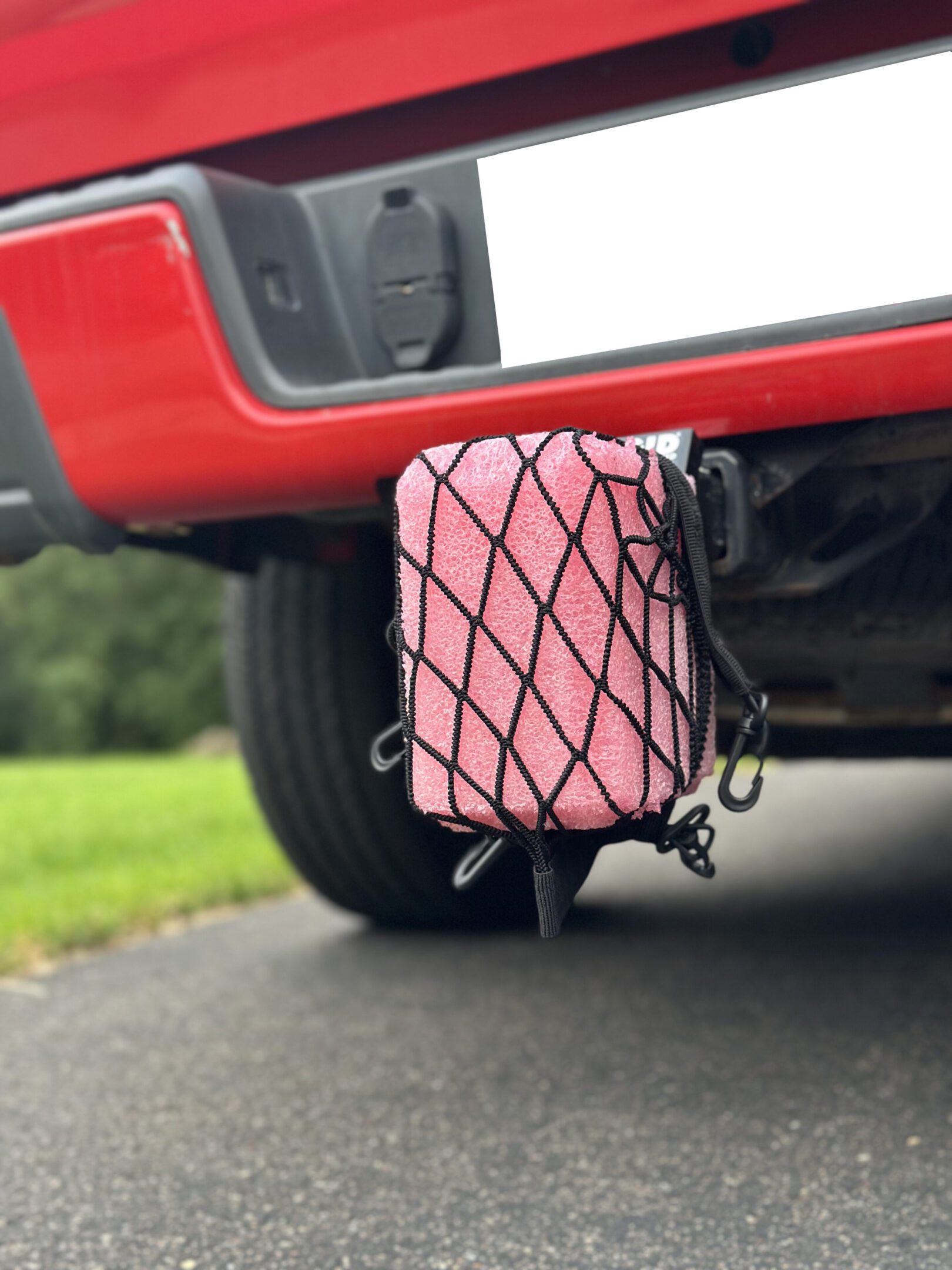 Pink cooler secured by netting on a vehicle's rear.