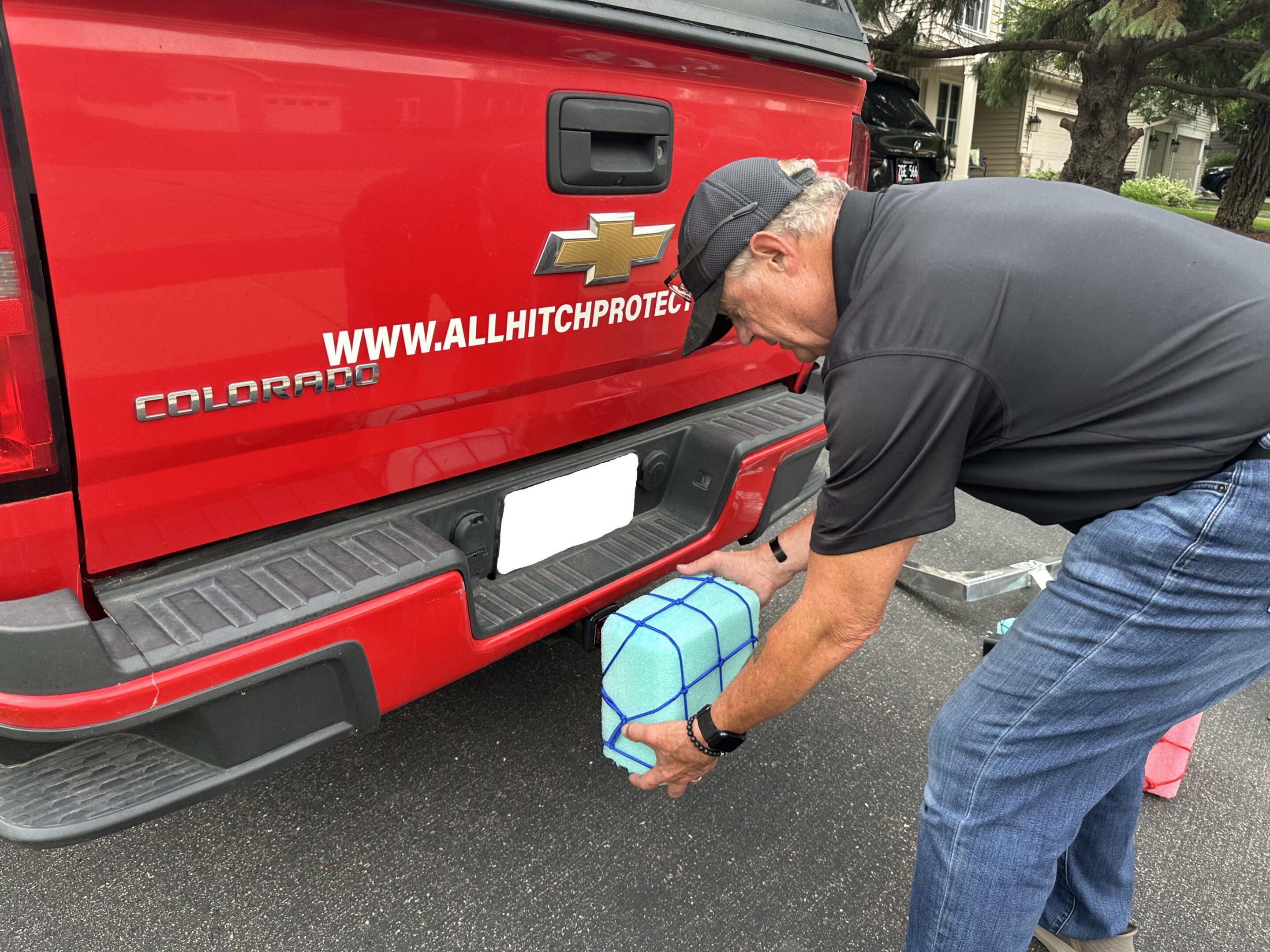 Man placing a blue wrapped gift on a red truck's bumper.