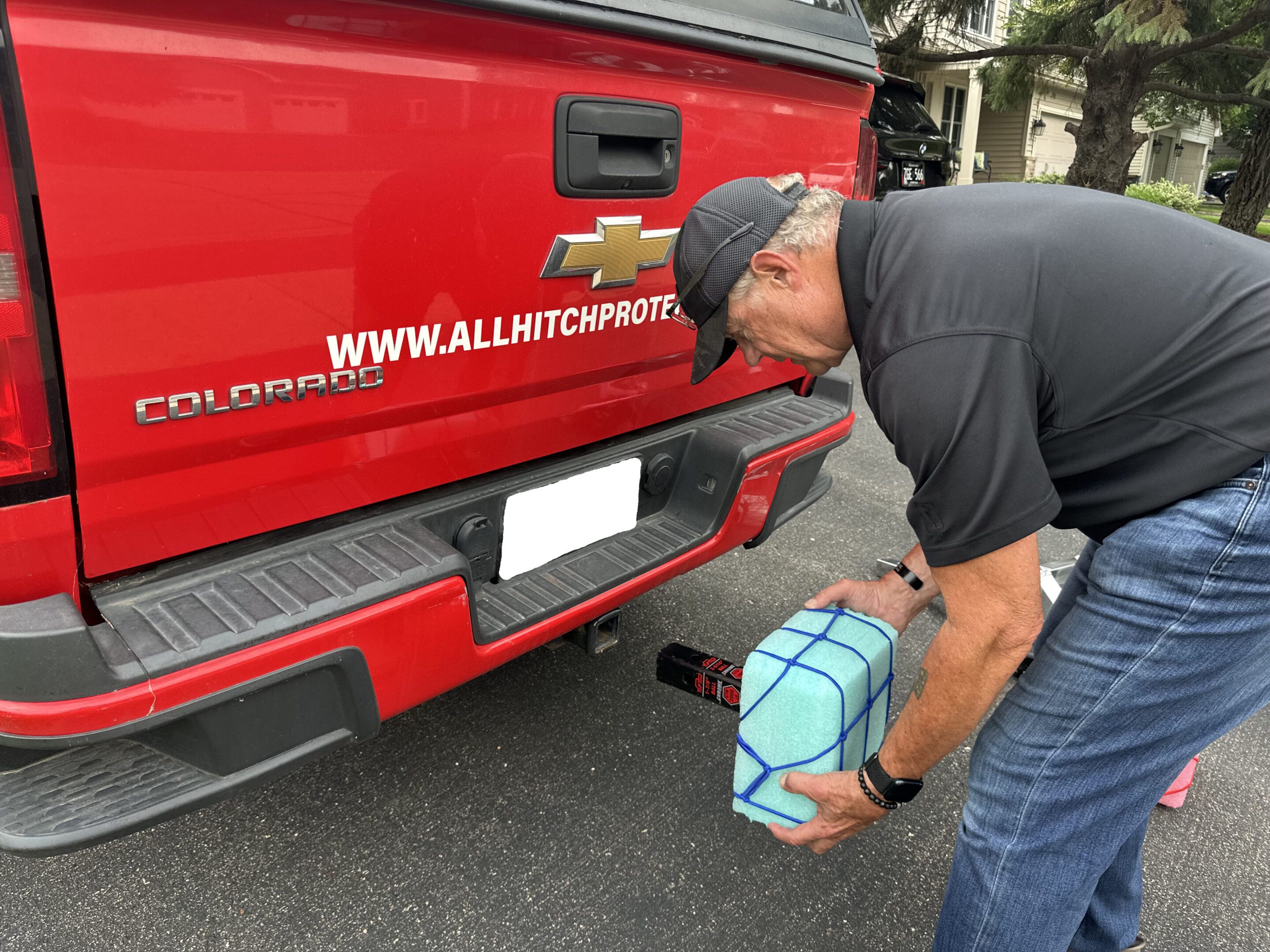 Man refilling red pickup truck's windshield washer fluid outdoors.