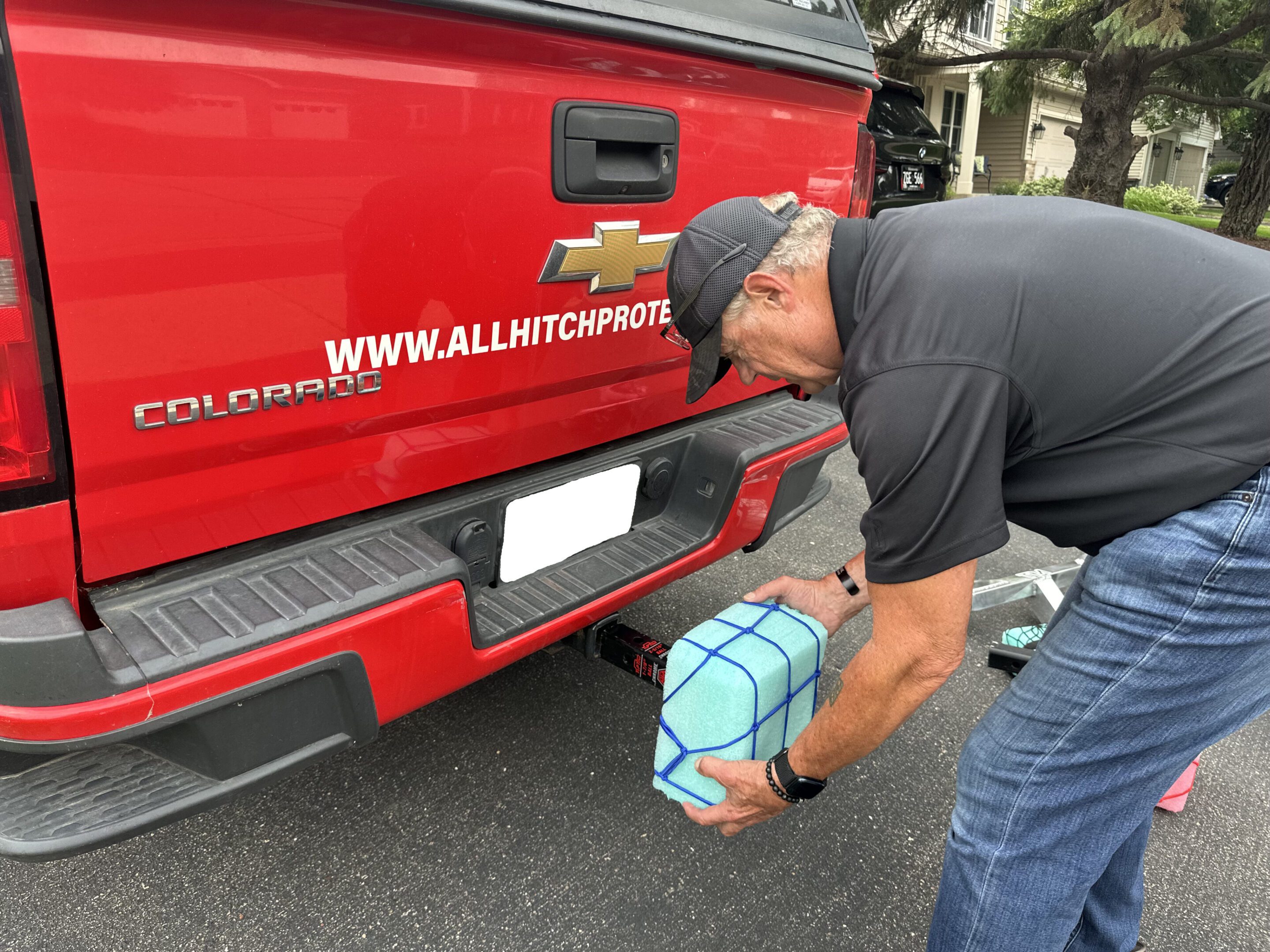Man tying blue luggage to the back of a red pickup truck.