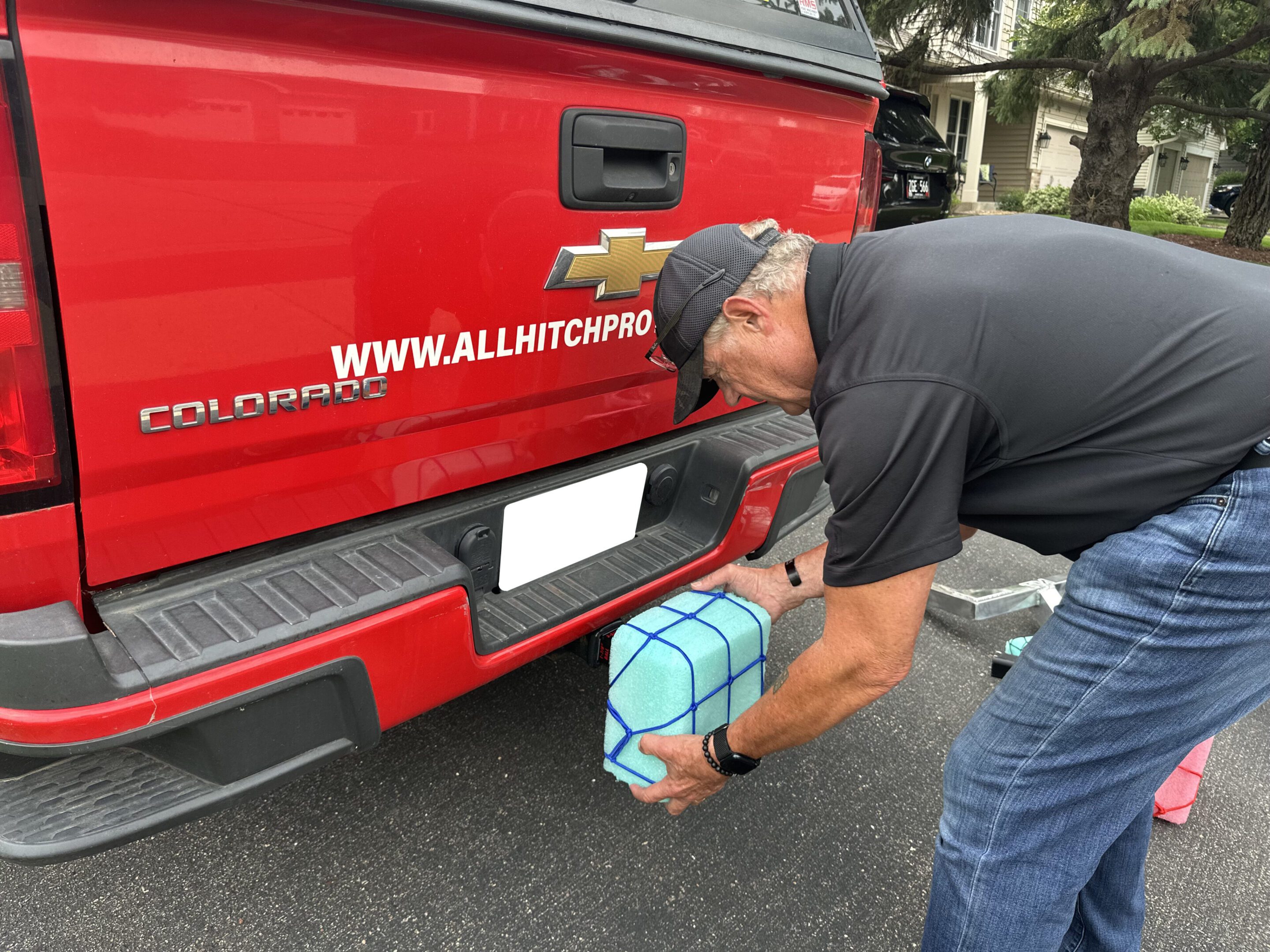 Man securing a blue gas can to the back of a red truck with a strap.