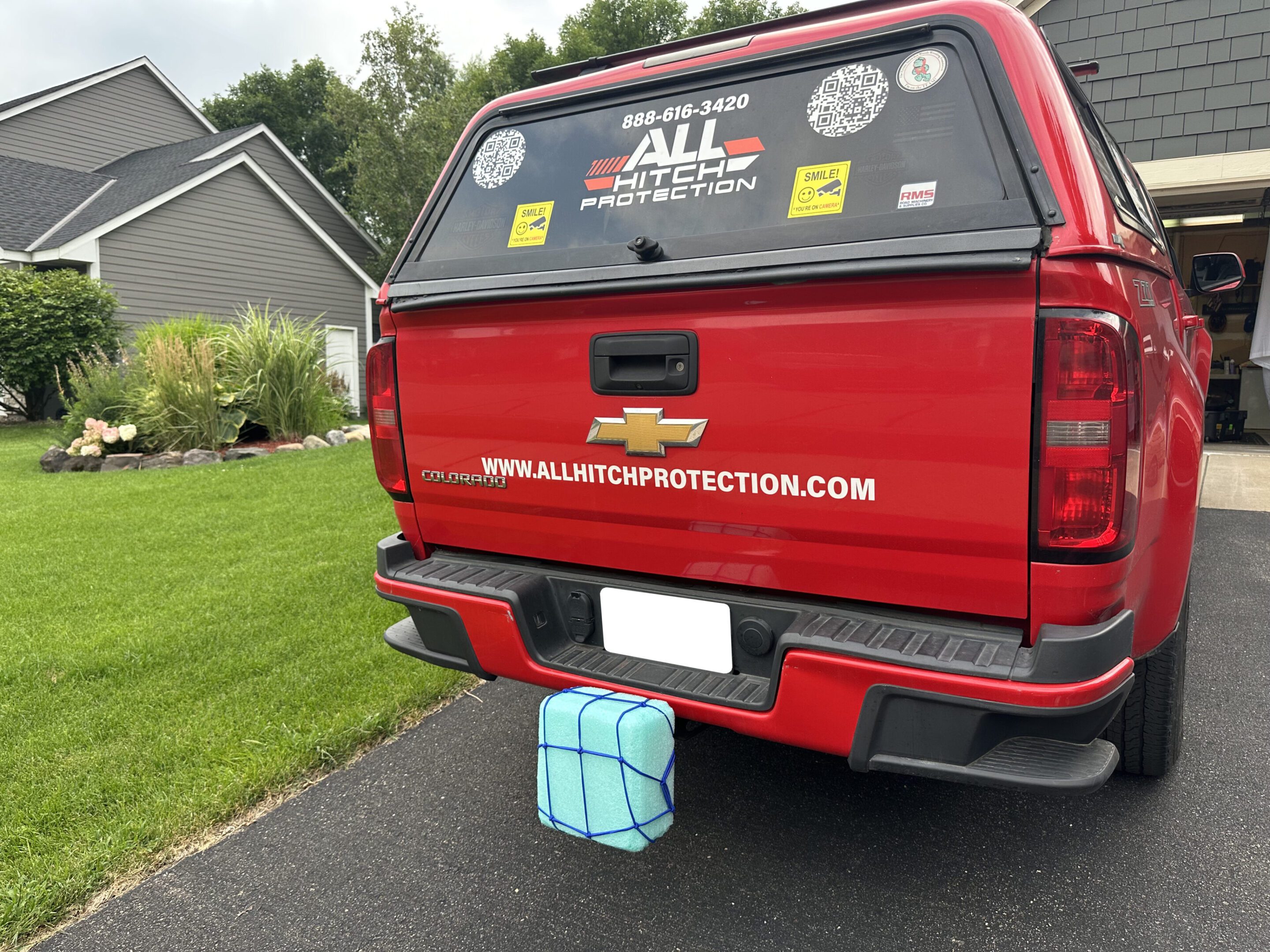 Red pickup truck with a large cube attached to its rear bumper in a suburban driveway.