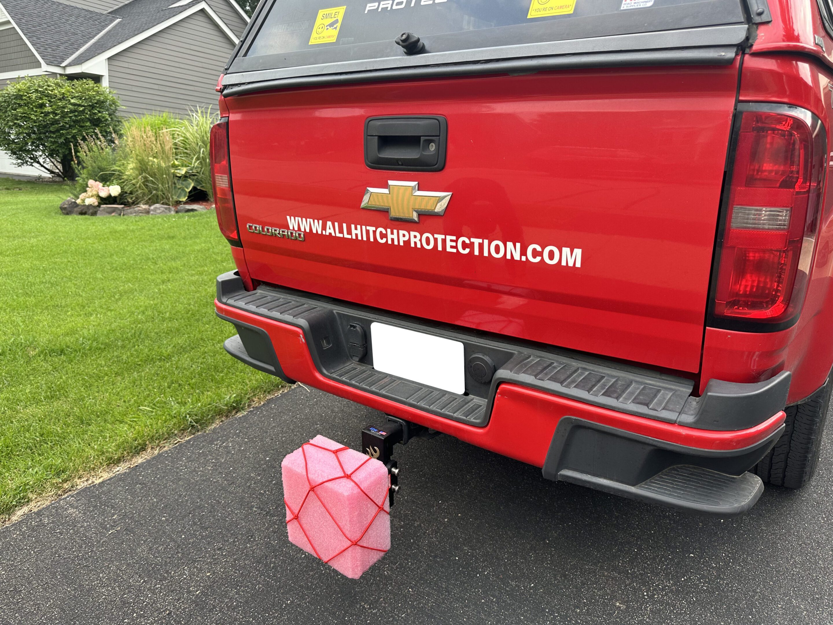 Red truck with a pink cube-shaped object hanging from the rear bumper.