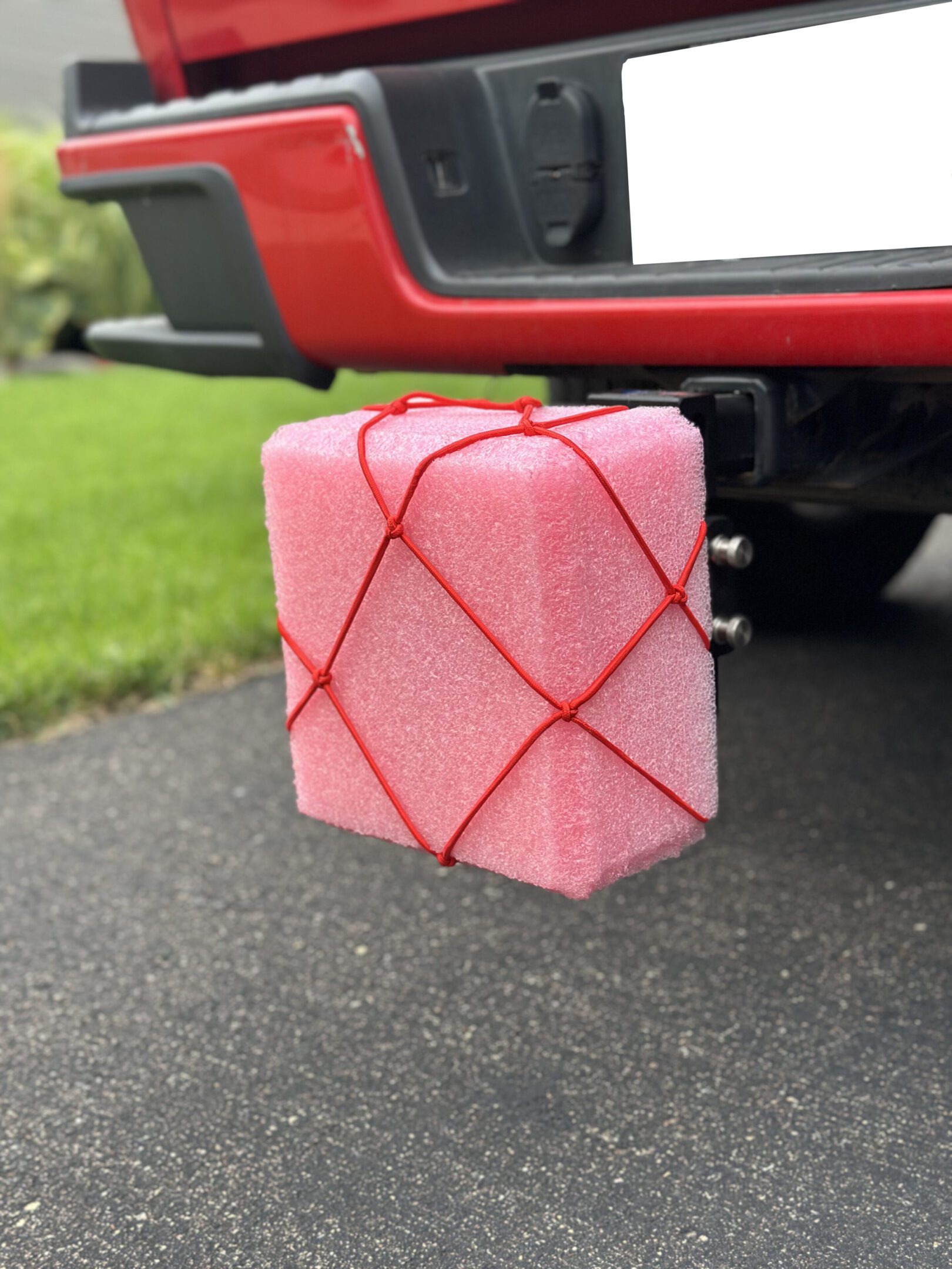 A pink foam block wrapped in red string hanging from a car hitch.