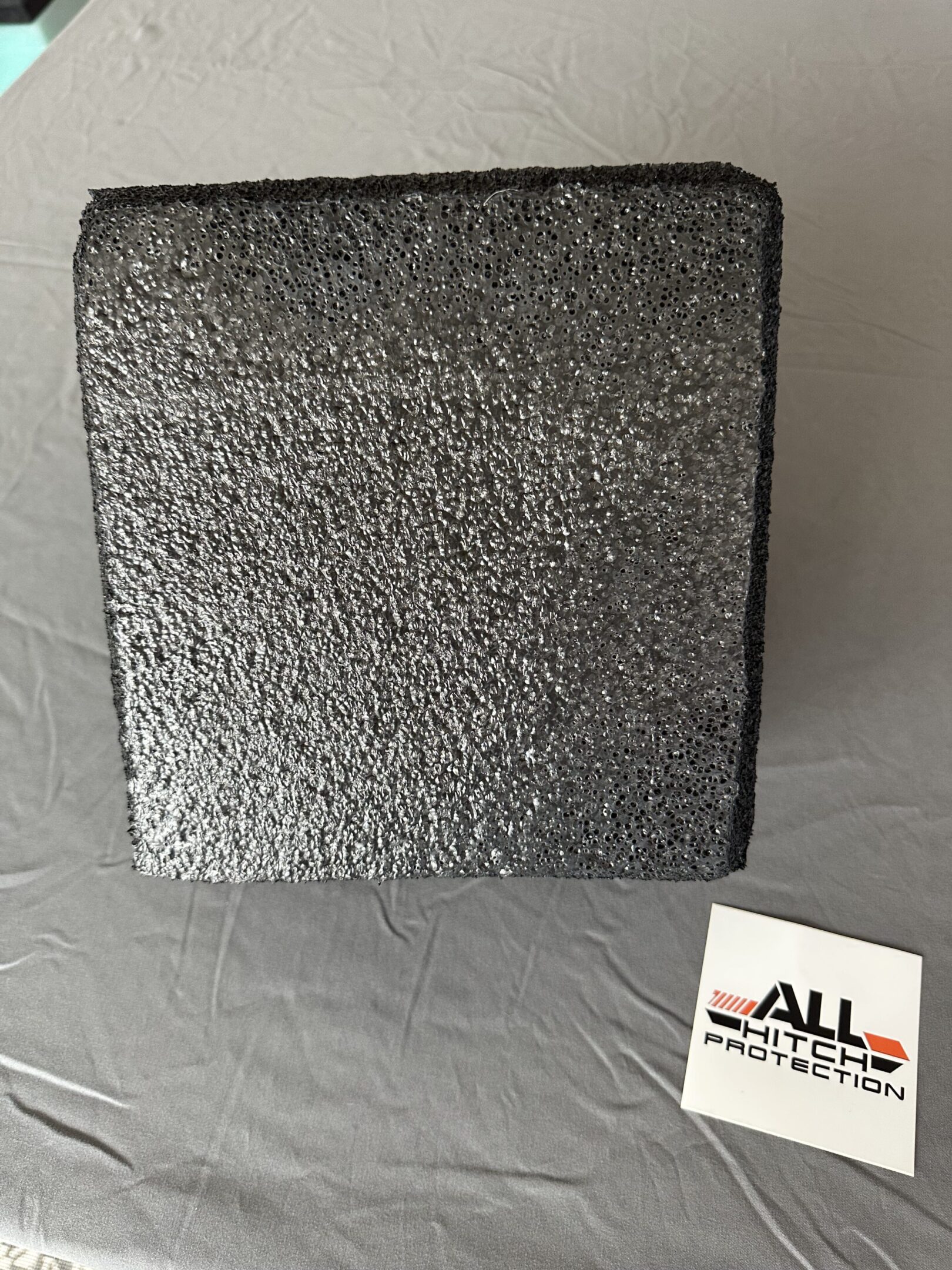 Close-up of a textured black square object on a gray surface.