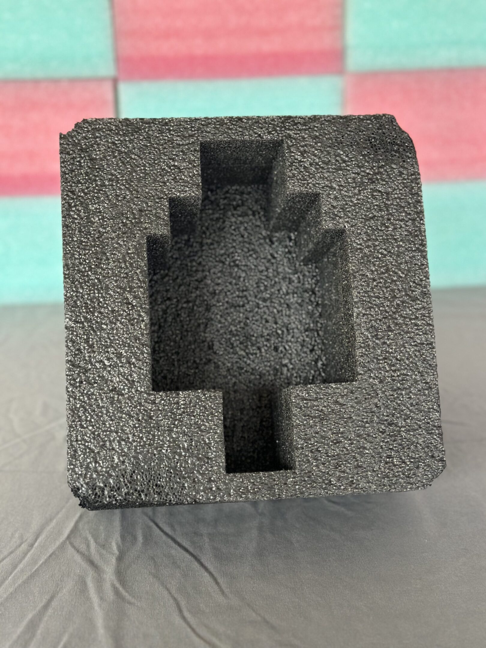 Black foam insert with a stepped rectangular cutout, placed on a colorful surface.