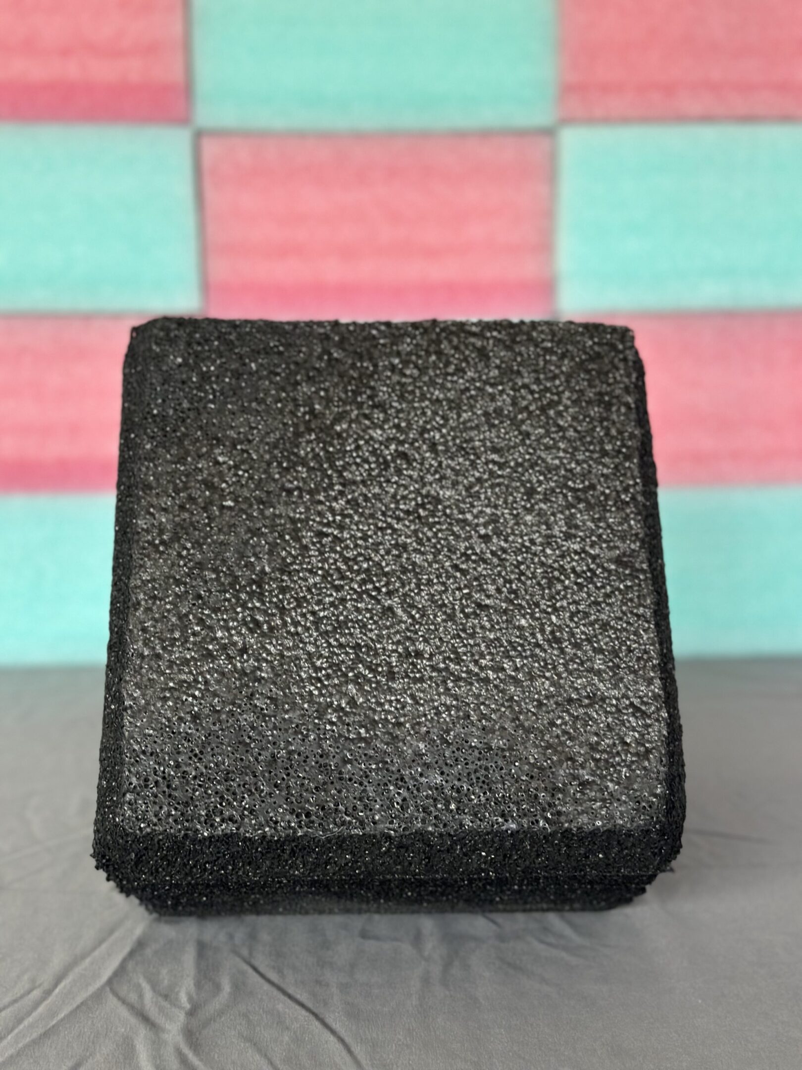 Close-up of a textured black square object on a colorful surface.