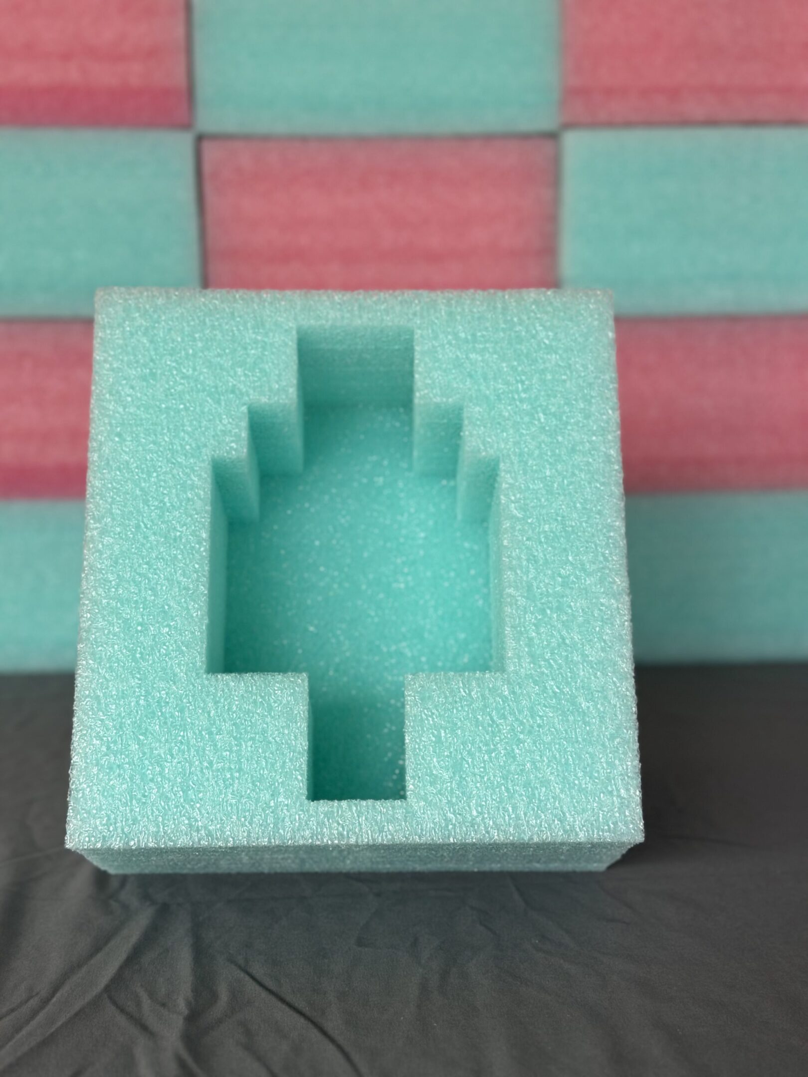 Green foam block with a cross-shaped cutout on a pink background.