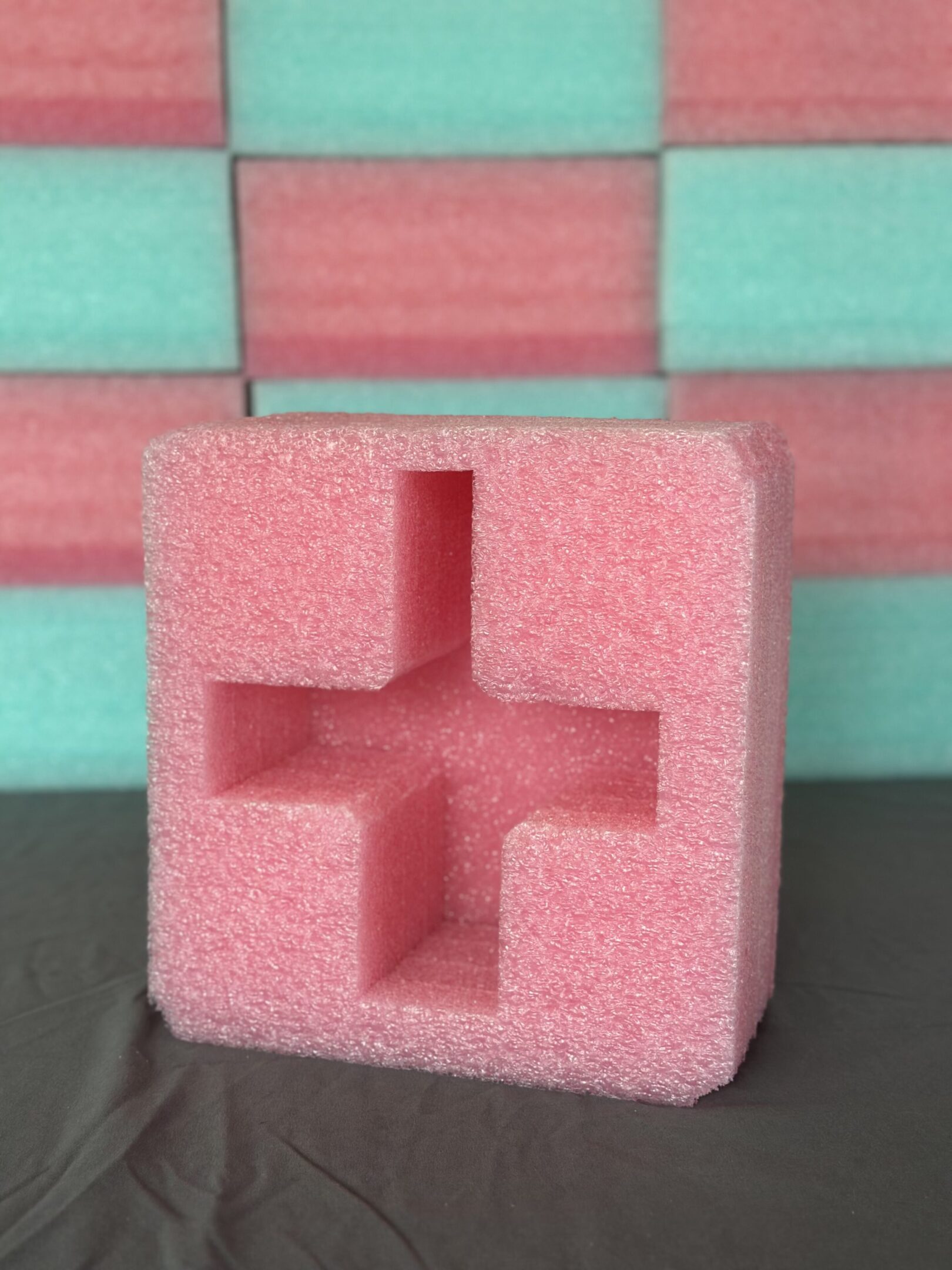 Pink foam block with a cross-shaped cutout on a wooden surface.