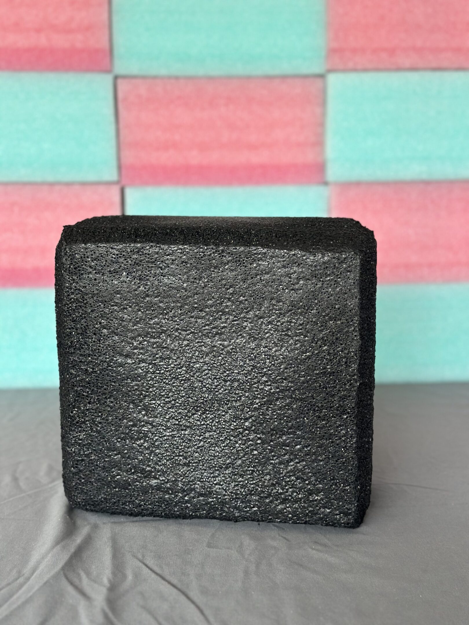 Black square-shaped wallet with textured surface on a gray base.