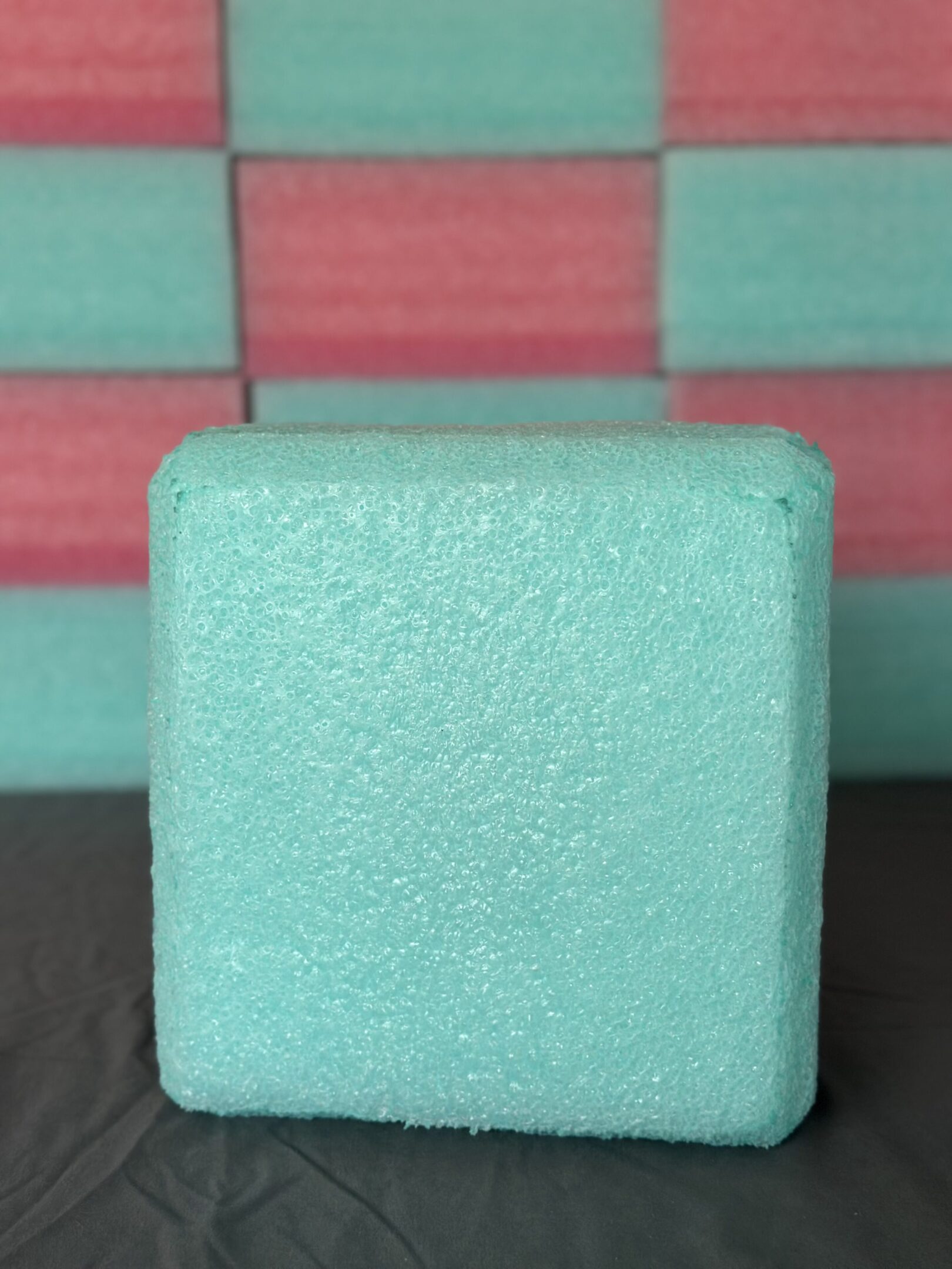 Close-up of a light blue textured cube against a red and teal background.
