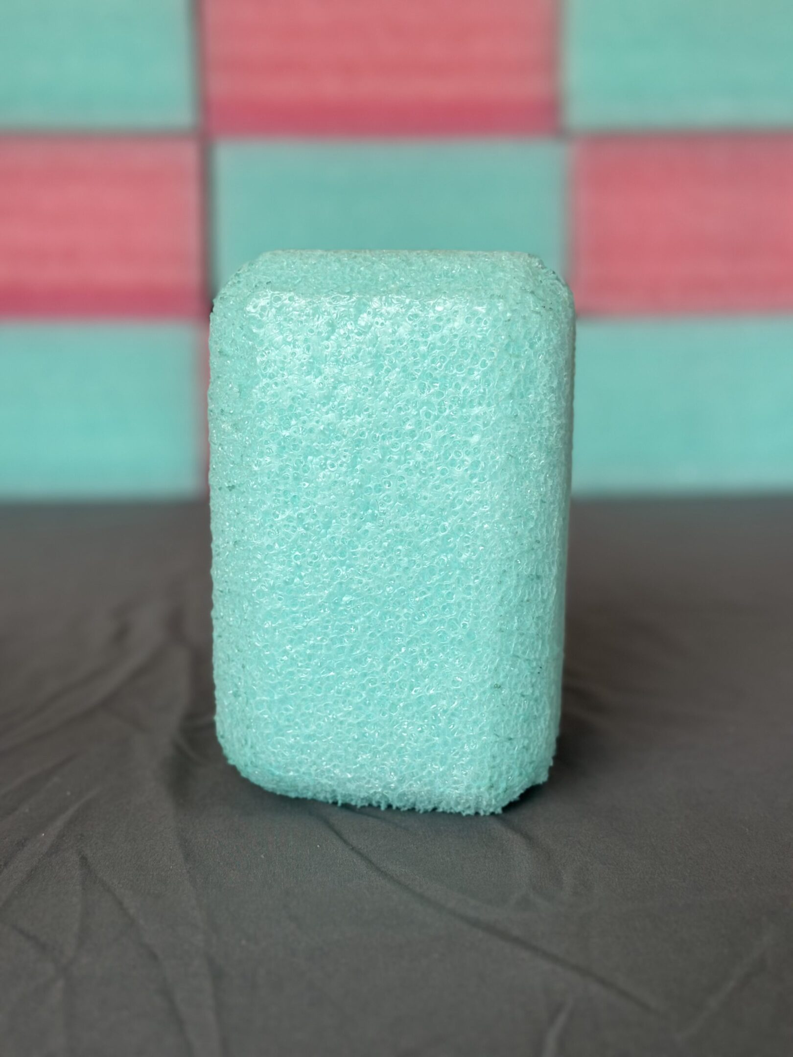 A close-up of a teal rectangular sponge on a dark surface.