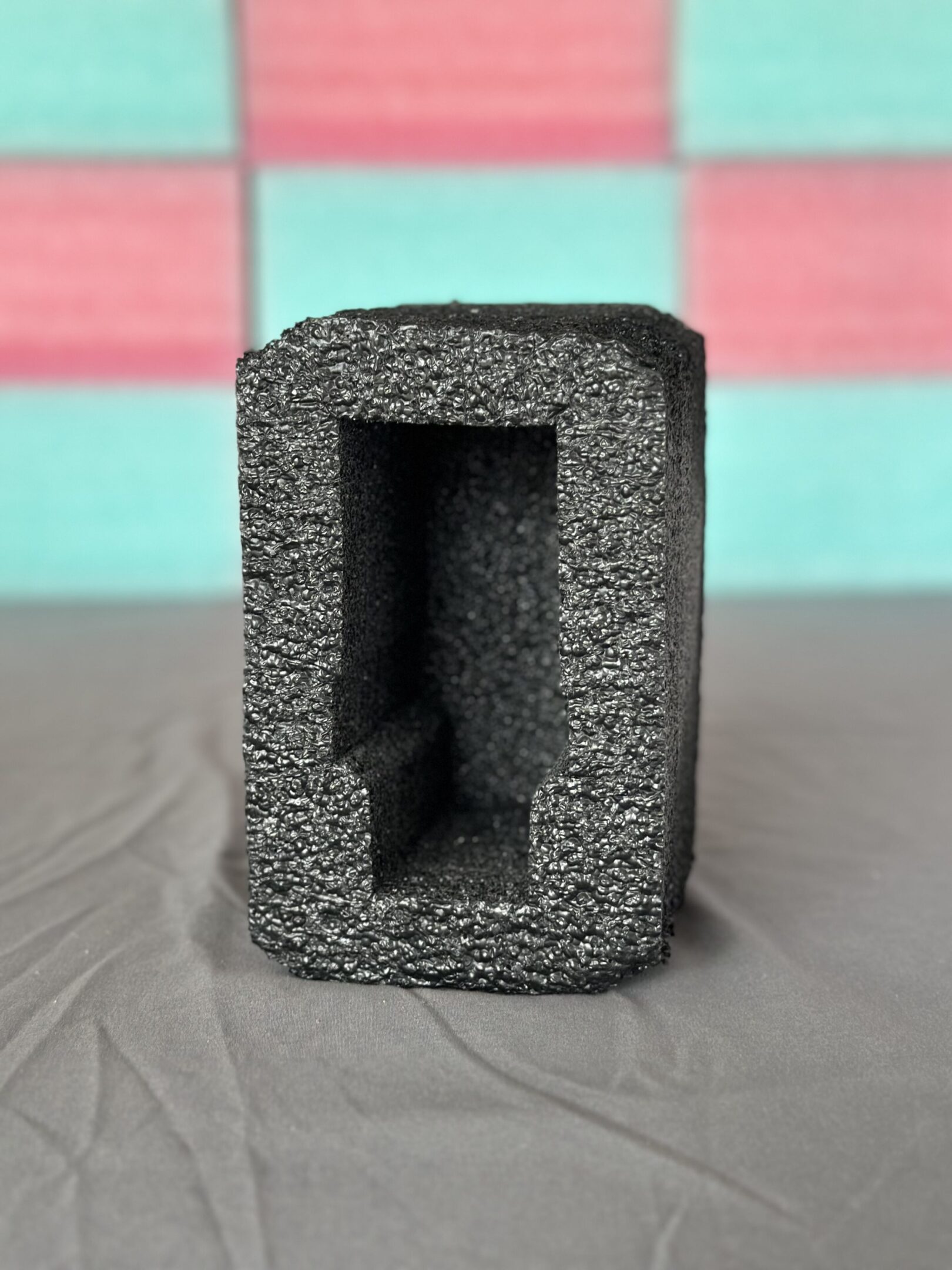 A gray rectangular foam block with a hollow center on a fabric surface.