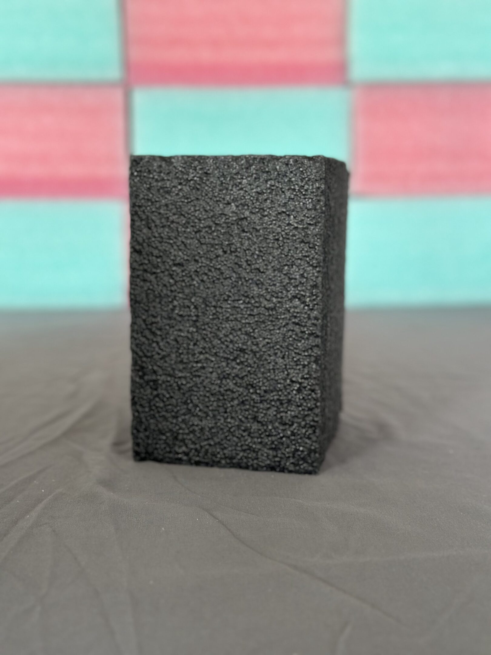 A black rectangular textured block on a gray surface with a colorful background.
