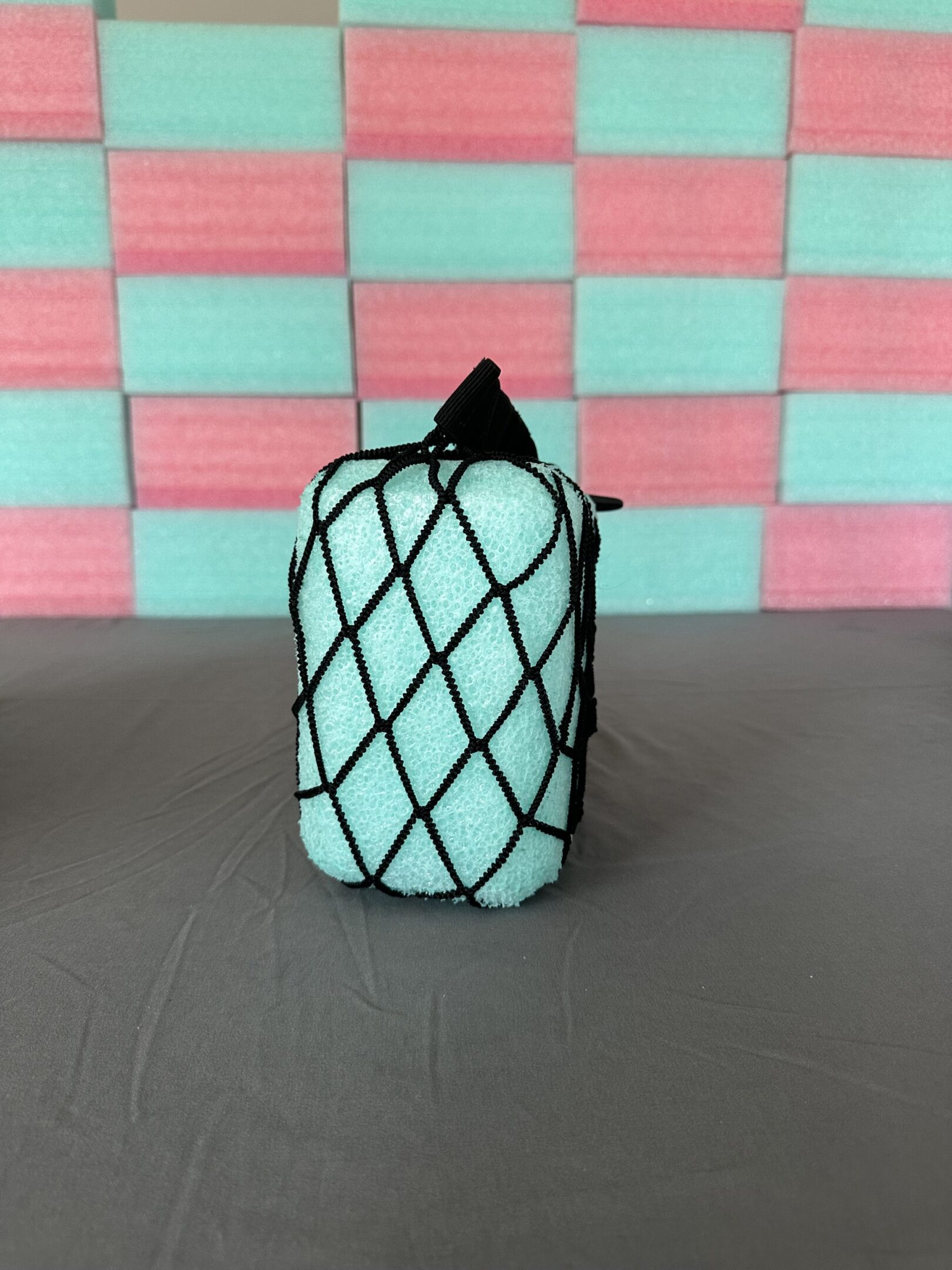 A mint green candle with black netting and a black wick on a gray surface.