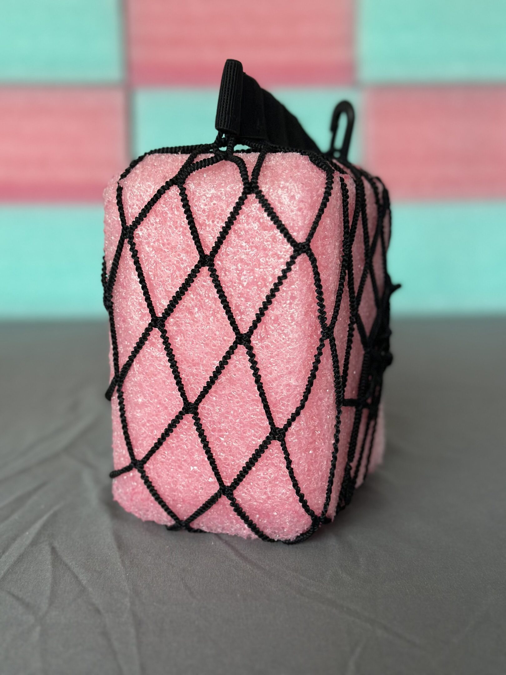 Pink towel wrapped in a black net, standing upright on a gray surface.