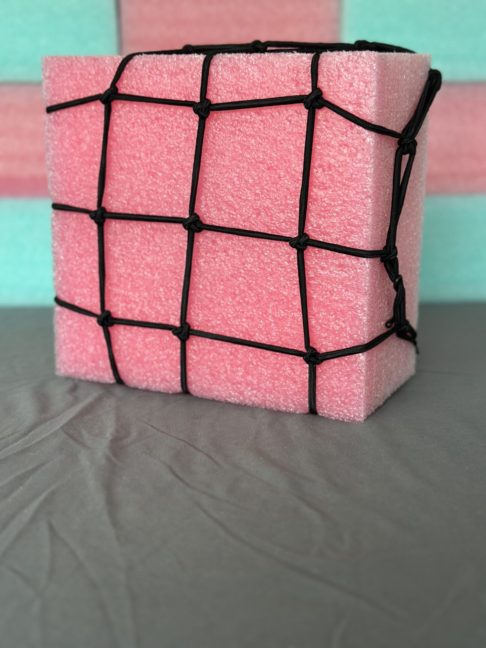 Pink foam block wrapped with black netting on gray fabric.