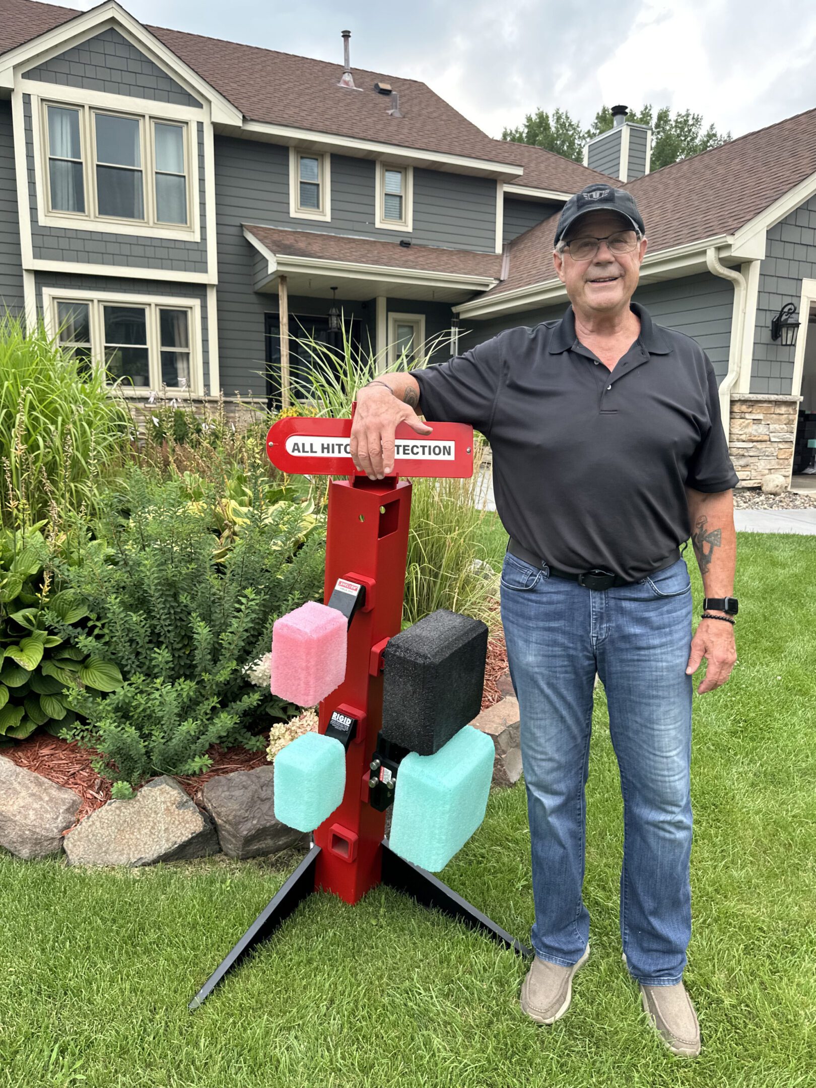 Man standing next to a red mailbox with colorful mailboxes in front of a house.
