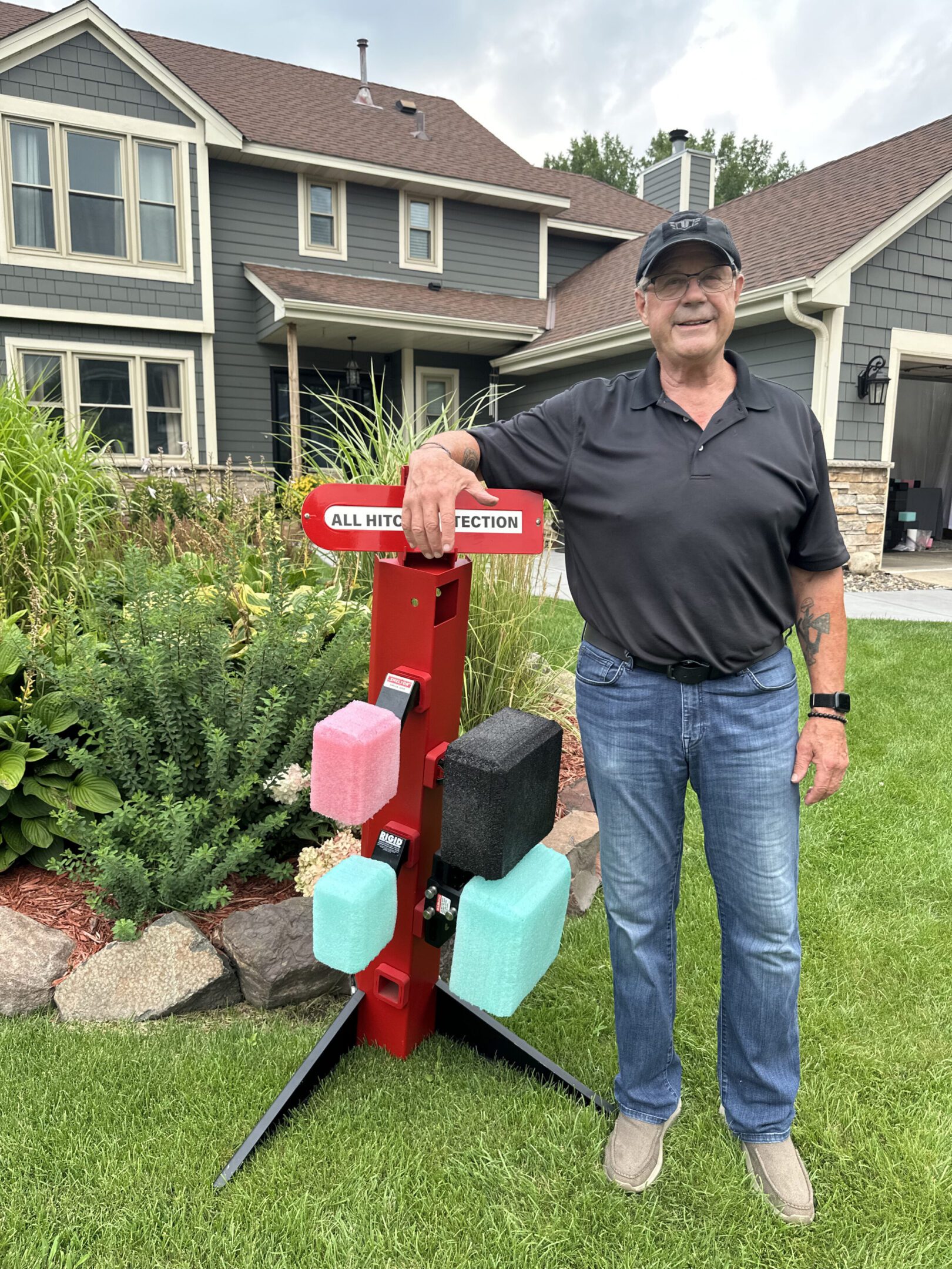 Man standing next to a wooden post with colorful birdhouses in front of houses.