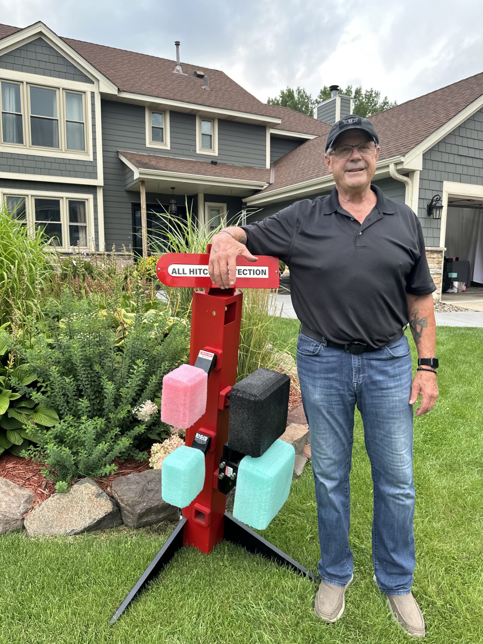Man standing next to a red mailbox with multiple compartments in a suburban neighborhood.