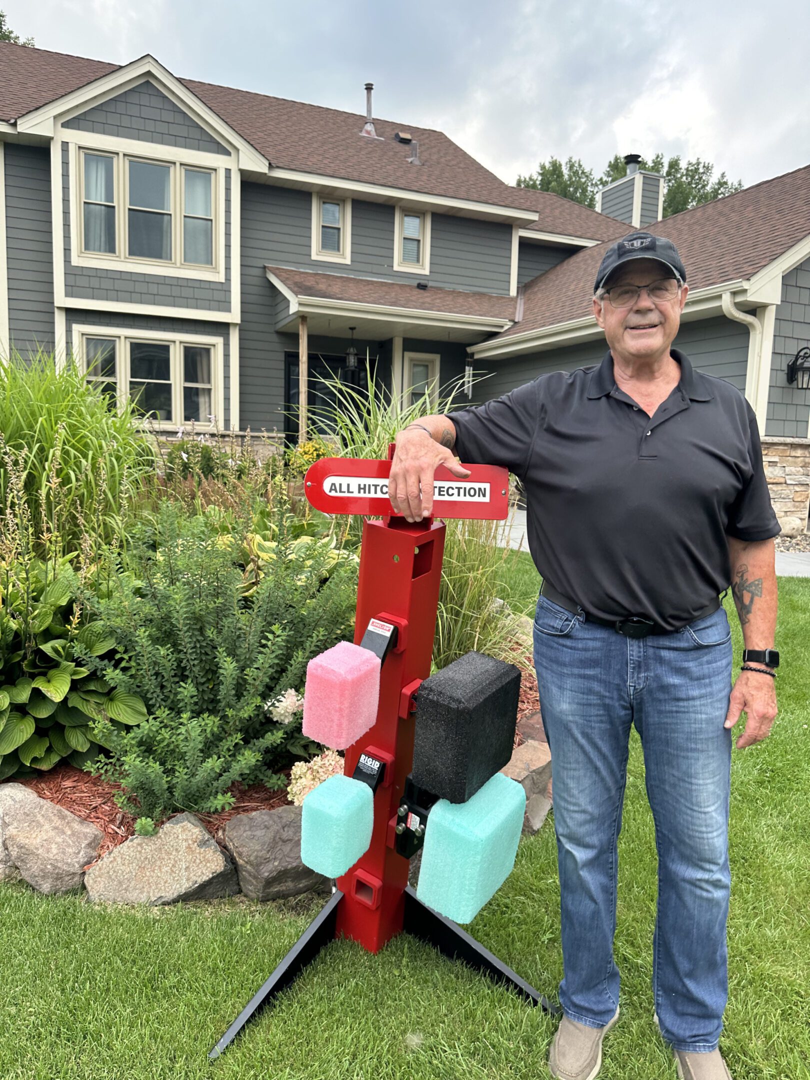 Man standing beside a colorful wooden mailbox post in a garden.