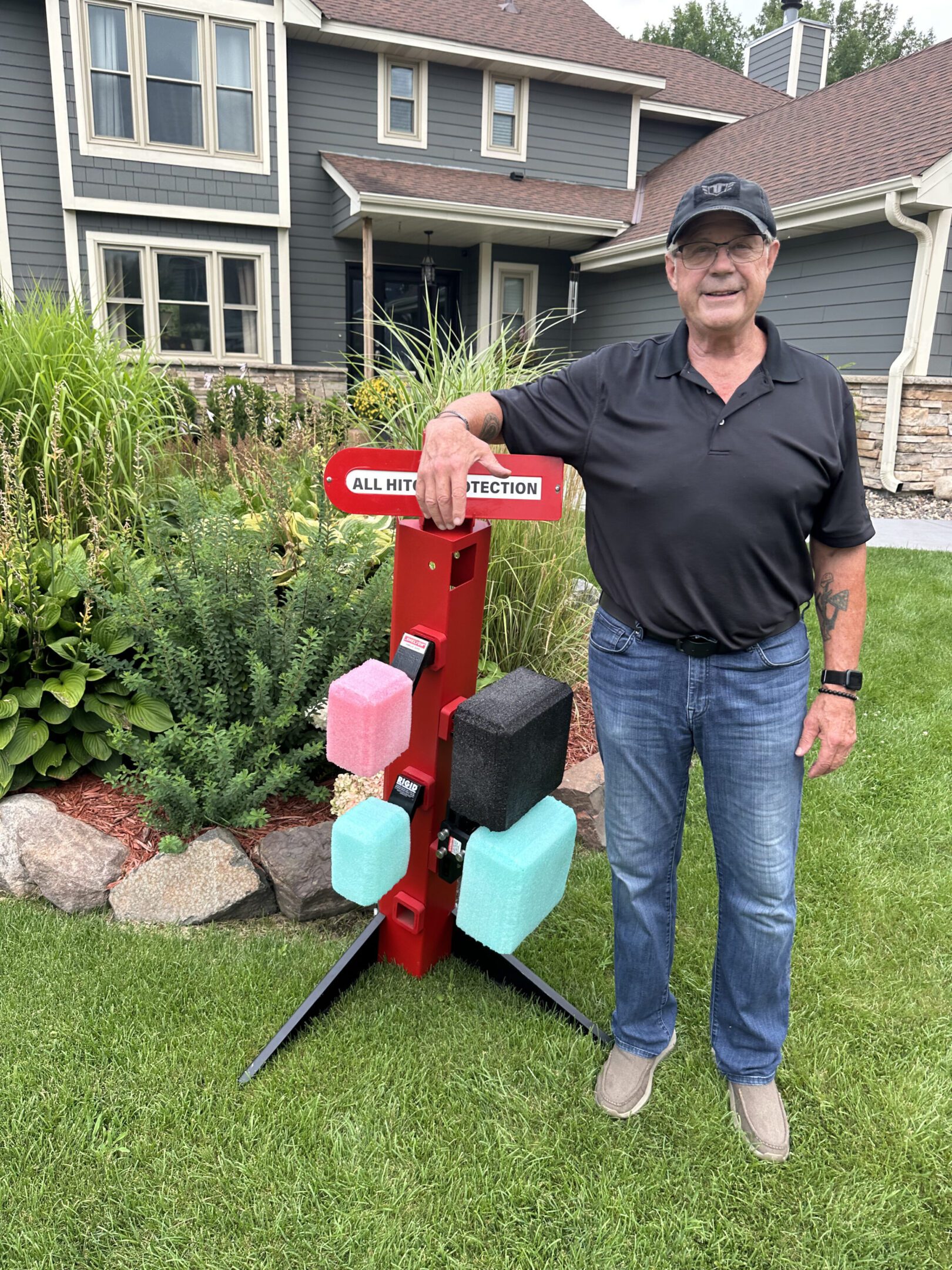 Man standing next to a colorful wooden cross in a garden.