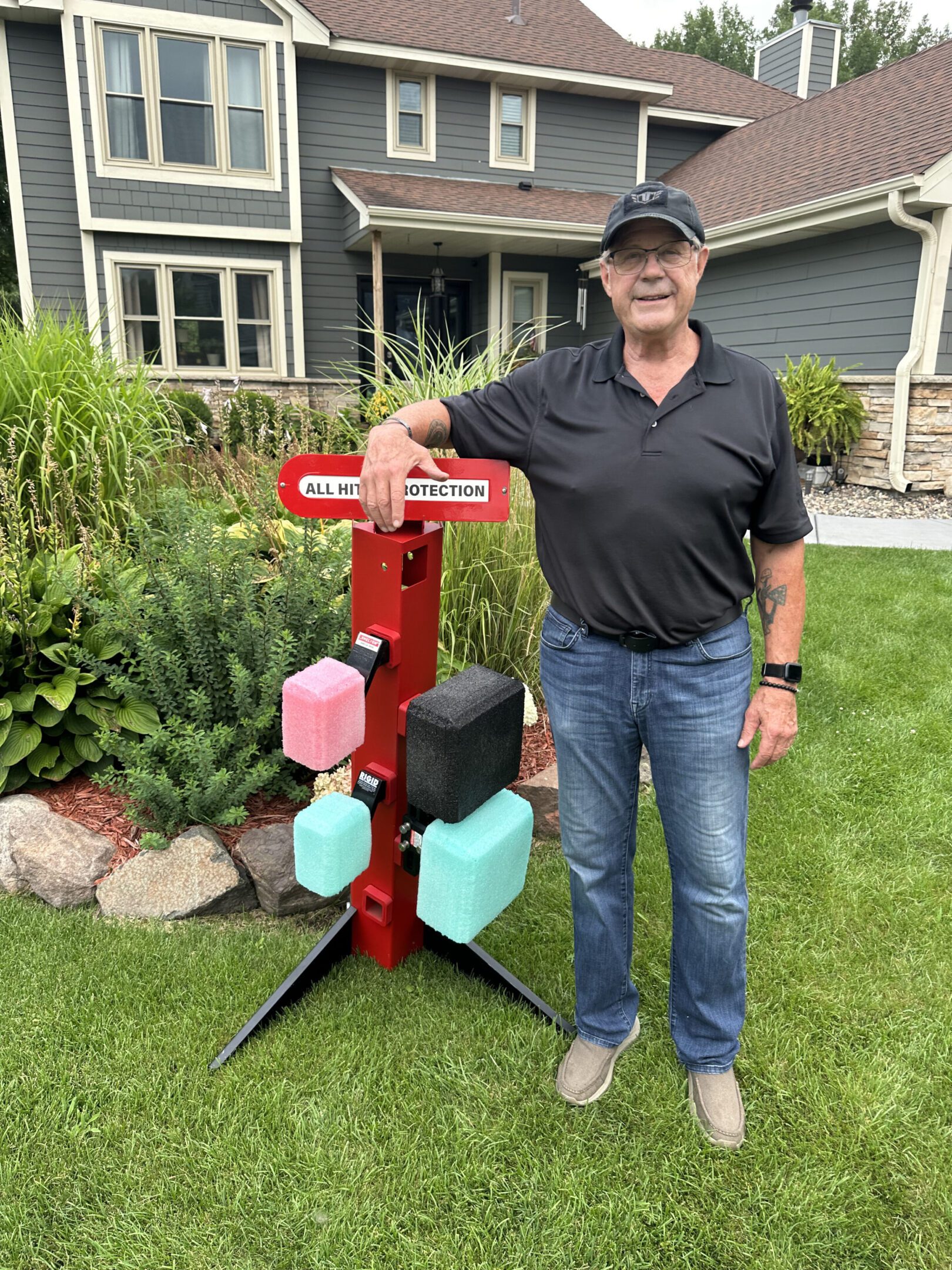 Man standing next to a colorful, handmade wooden birdhouse in a garden.